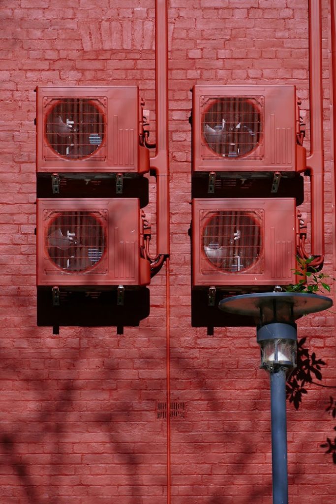 Red air conditioning units on a red brick wall in Adelaide, emphasizing urban architecture.