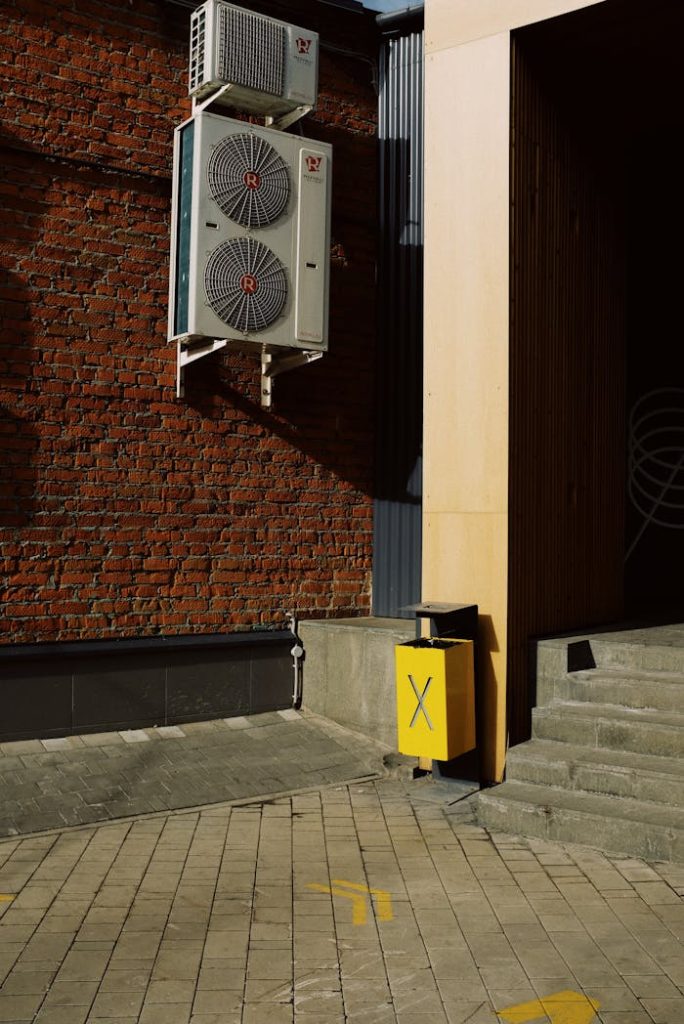 Modern exterior with HVAC units on a brick wall and a yellow waste bin near stairs.